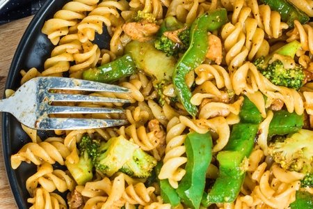 A close-up shot of a fork digging into a plate of whole wheat fusilli pasta mixed with vibrant broccoli florets and crisp green beans.の写真素材