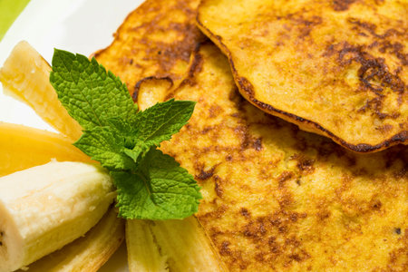 Close-up of fluffy sweet potato pancakes served with sliced banana and a sprig of fresh mint, a delicious and healthy breakfast.の写真素材