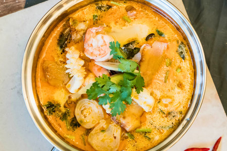 A close-up overhead view of a rich, creamy Thai coconut curry soup filled with succulent shrimp and vibrant vegetables, garnished with fresh cilantro.の写真素材