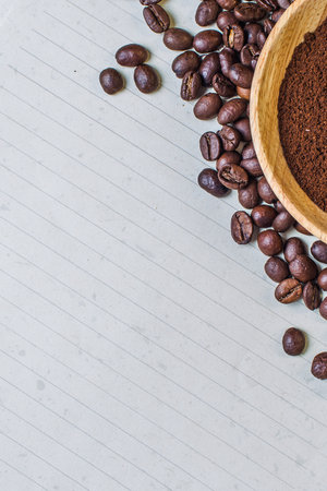 A textured surface displays scattered roasted coffee beans and a portion of ground coffee in a wooden bowl.の写真素材