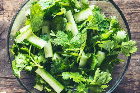 A vibrant bowl of fresh salad featuring crisp cucumber pieces and fragrant cilantro, presented on a rustic wooden surface.の写真素材