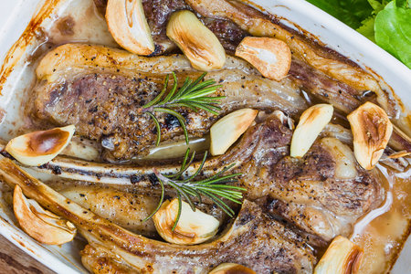 Close-up of succulent, golden-brown roasted lamb chops seasoned with herbs and garlic, presented in a white dish.の写真素材