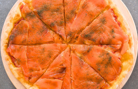 A close-up overhead view of a freshly baked pizza generously topped with thin slices of salmon and sprinkled with herbs.の写真素材