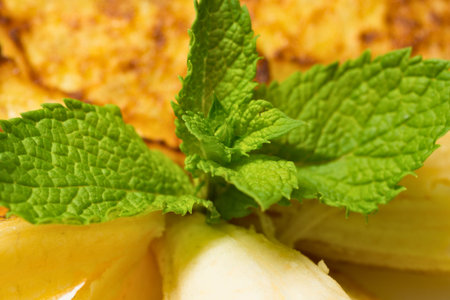 Close-up of vibrant green mint leaves topping a sweet dessert, possibly featuring pineapple chunks and a crunchy topping.の写真素材