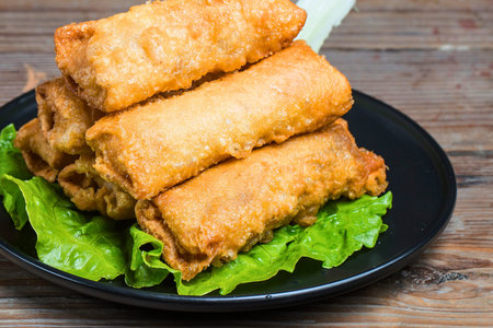 A close-up shot of a black plate filled with crispy, golden brown fried egg rolls served on a bed of...