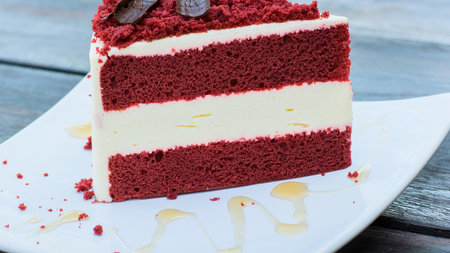 A rich slice of red velvet cake with thick layers of creamy white frosting, presented on a white plate.の写真素材