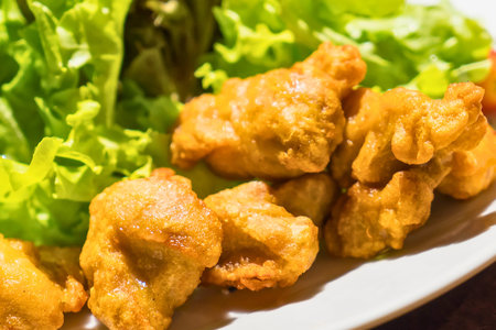 A close-up shot of golden brown, crispy fried chicken pieces arranged next to vibrant green lettuce leaves on a white plate.の写真素材