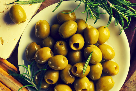 A close-up shot of a white bowl filled with plump green olives, garnished with fresh rosemary sprigs and a hint of cheese.の写真素材