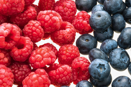A detailed, overhead view of ripe, red raspberries next to plump, blue blueberries, showcasing their textures and colors.の写真素材