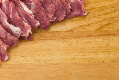 Thinly sliced raw meat, likely beef or pork, is arranged on a light-colored wooden cutting board, ready for preparation.の写真素材