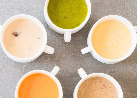 A top-down view of five white ceramic cups filled with various colorful creamy sauces, arranged in a circular pattern on a textured surface.の写真素材