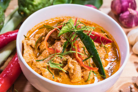 A close-up overhead shot of a vibrant bowl of Thai red curry, garnished with fresh herbs and chilies.の写真素材
