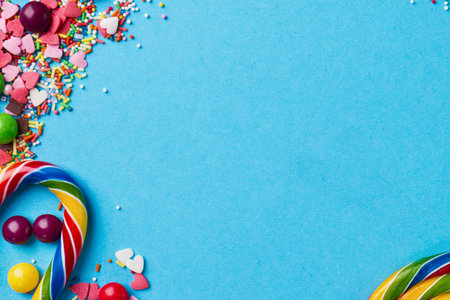 A vibrant collection of candies, including a rainbow lollipop, gumdrops, and sprinkles, arranged on a bright blue surface.の写真素材