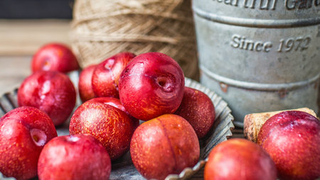 A close-up shot of vibrant, juicy red plums artfully arranged in a decorative bowl, with rustic elements in the background.の写真素材