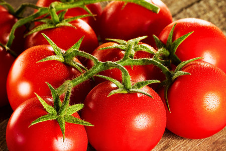 A close-up view of numerous vibrant, ripe red tomatoes with green stems, showcasing their fresh, natural beauty.の写真素材