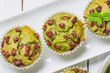 Close-up view of three vibrant green matcha muffins topped with red beans and a sprig of mint, presented on a white platter.の写真素材