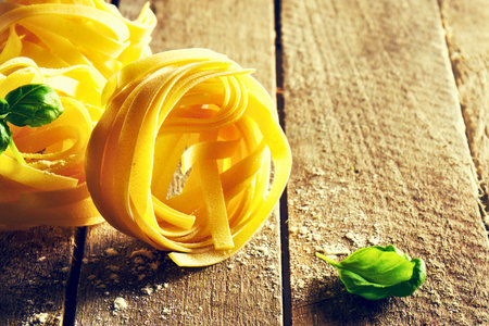 Close-up of golden pasta nests with fresh basil leaves and a sprinkle of salt on a weathered wooden table.の写真素材