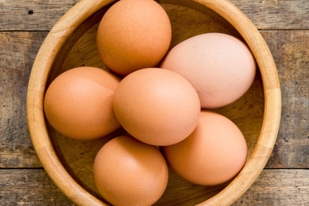 A top-down view of six brown eggs nestled within a wooden bowl, resting on a weathered wooden surface.の写真素材