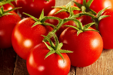A close-up shot of vibrant red tomatoes still attached to their green stems, showcasing their natural beauty and freshness.の写真素材