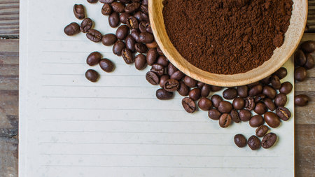A rustic overhead view of roasted coffee beans scattered next to a wooden bowl filled with finely ground coffee.の写真素材