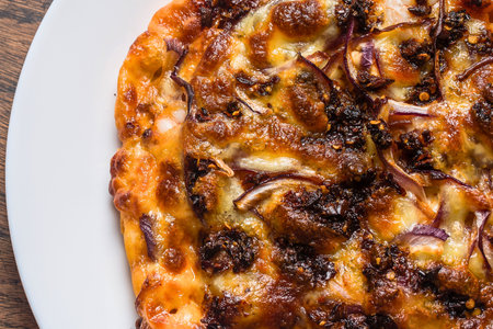 A close-up, overhead view of a golden-brown pizza with visible caramelized onions and gooey melted cheese on a white plate.の写真素材