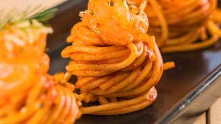 Close-up of perfectly twirled spaghetti nests coated in a rich orange sauce, presented elegantly on a dark platter.の写真素材