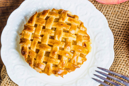 A delicious golden brown apple pie slice with a woven lattice crust sits on a white plate, ready to be enjoyed.の写真素材