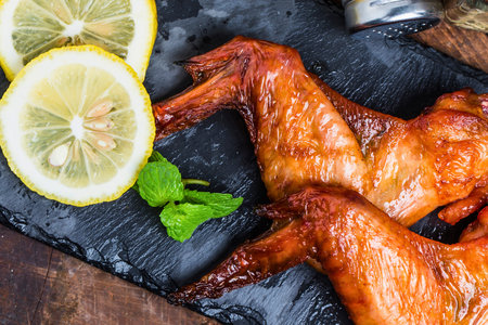 Close-up of perfectly smoked chicken wings served with vibrant lemon slices and fresh mint leaves on a dark slate surface.の写真素材