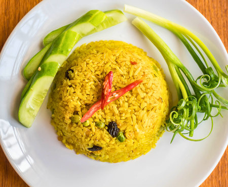A vibrant mound of yellow rice topped with red chili and served with fresh green vegetables on a white plate.の写真素材