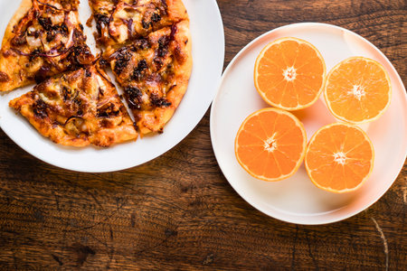 A top-down view of a partially eaten pizza and four bright orange slices on white plates, set against a textured wooden background.の写真素材