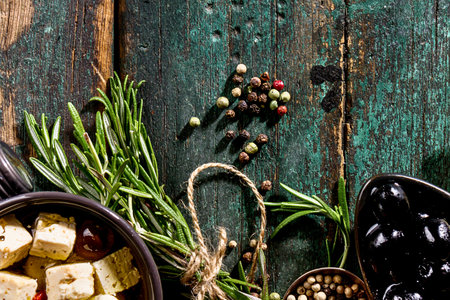 A close-up view of fresh rosemary, peppercorns, and olives arranged on a weathered, textured wooden background.の写真素材
