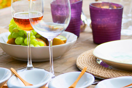 A beautifully arranged outdoor table setting features wine glasses, a bowl of fruit, and decorative elements, perfect for a gathering.の写真素材