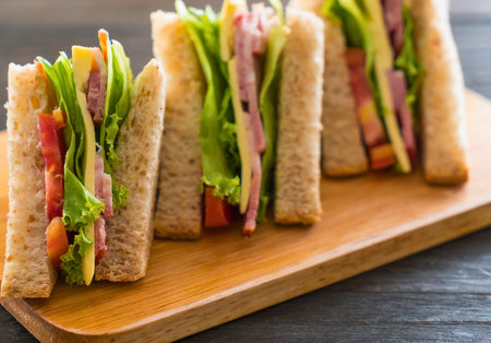 A close-up view of several stacked club sandwiches with fresh ingredients, presented on a rustic wooden board.の写真素材