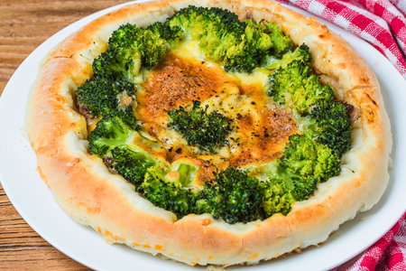 A delicious broccoli and cheese tart with a flaky golden crust sits on a white plate, ready to be served.の写真素材