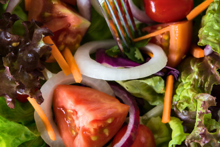 A close-up shot of a vibrant, healthy salad featuring fresh lettuce, juicy tomatoes, crisp carrots, and sliced red onion.の写真素材