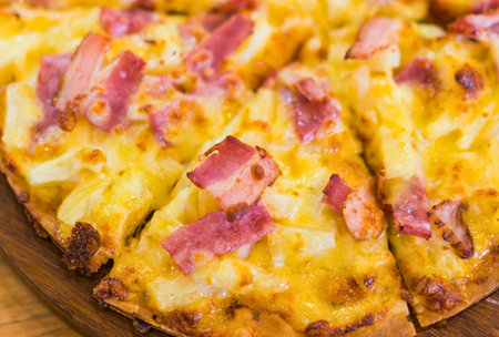 A mouthwatering close-up of a freshly baked Hawaiian pizza, featuring golden cheese, savory ham, and sweet pineapple chunks.の写真素材