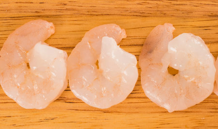 Close-up view of three uncooked, peeled shrimp lined up horizontally on a textured wooden board, ready for cooking.の写真素材