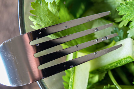 A close-up shot of a metal fork ready to pick up fresh green salad leaves and herbs for a healthy meal.の写真素材
