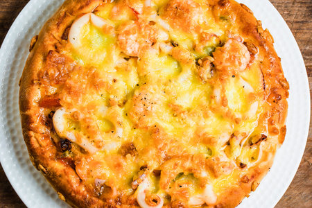 A close-up overhead view of a perfectly cooked, golden brown omelette filled with colorful vegetables and topped with melted cheese.の写真素材