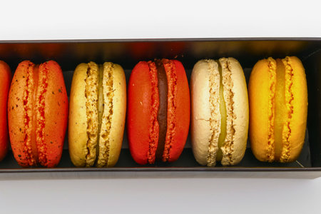 A close-up shot of a row of vibrant macarons in various colors, neatly arranged in a dark rectangular tray.の写真素材