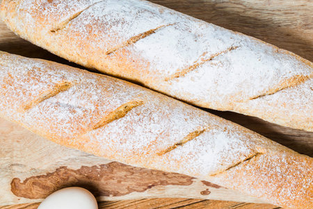 Close-up view of two golden-brown baguettes dusted with flour, showcasing their crusty texture and diagonal score marks.の写真素材