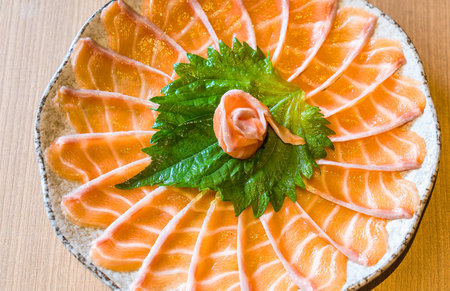 A vibrant platter of thinly sliced salmon sashimi arranged in a circular pattern around a fresh green garnish.の写真素材