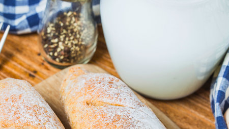 Two neatly wrapped sandwiches sit on a wooden board beside a pepper shaker and a checkered cloth, suggesting a wholesome meal.の写真素材
