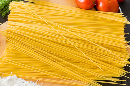 A close-up view of a large bundle of dry spaghetti pasta, with vibrant red tomatoes and green herbs in the background.の写真素材