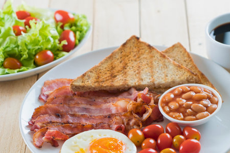 A delicious and filling breakfast featuring crispy bacon, fried egg, toasted bread, baked beans,...