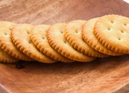 A close-up shot of several golden round cheese crackers arranged in a row on a textured wooden background.の写真素材