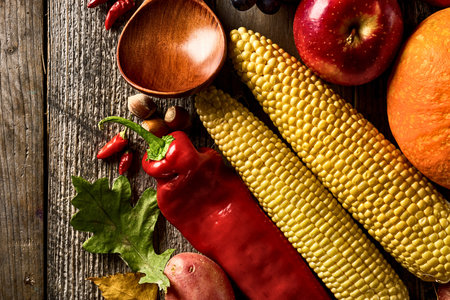 A vibrant assortment of fresh produce including corn, peppers, apples, and squash arranged on a weathered wooden surface.の写真素材