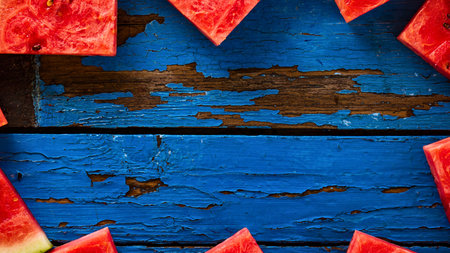 Juicy red watermelon pieces are arranged around a textured, weathered blue wooden background, creating a refreshing summer visual.の写真素材