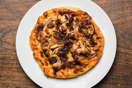 A rustic flatbread pizza, perfectly toasted and topped with savory caramelized onions and melted cheese, served on a white plate.の写真素材