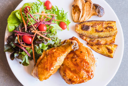 A white oval plate holds a hearty meal of roasted chicken, a fresh green salad, and sweet fried plantains, perfect for a satisfying lunch or dinner.の写真素材